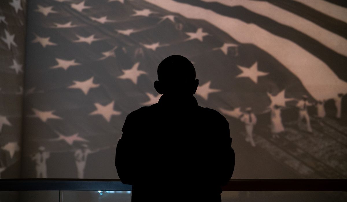 Silhouette of person against large American flag display background.