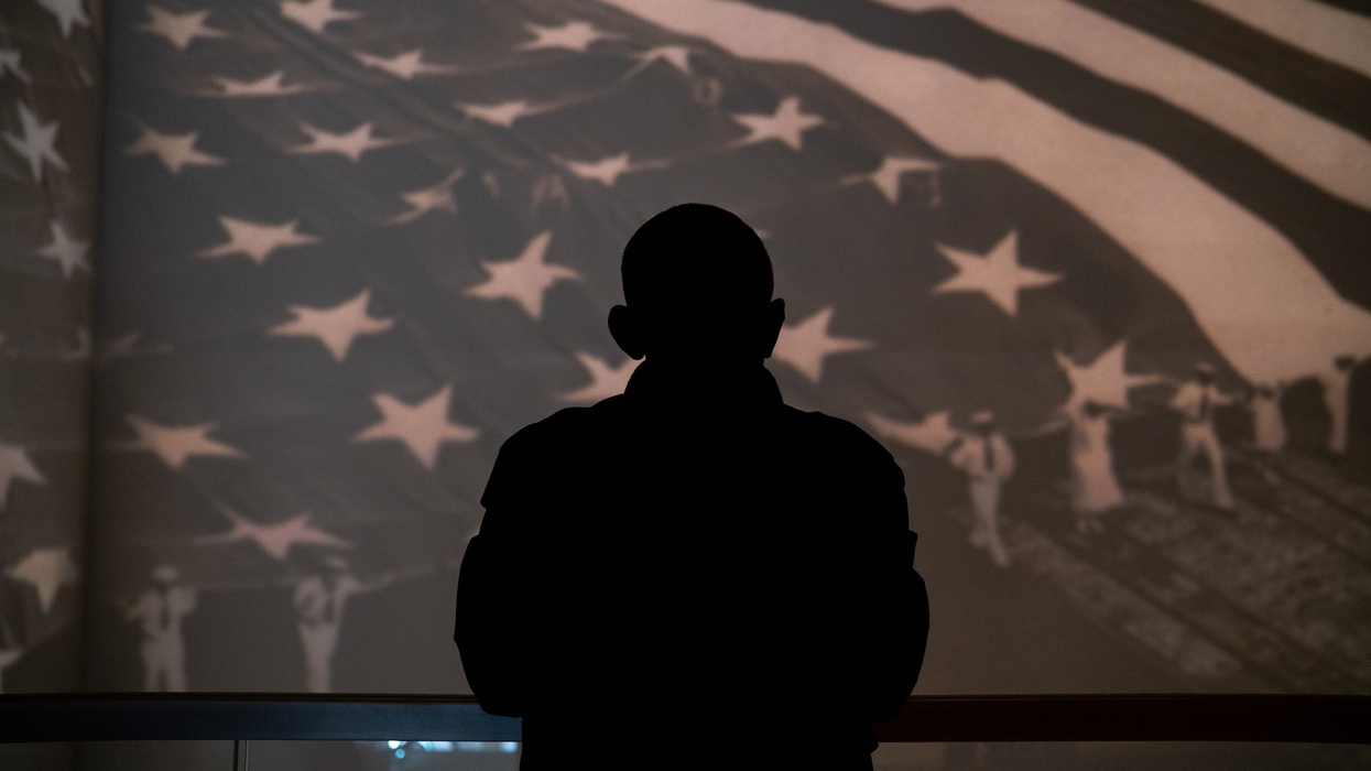 Silhouette of person against large American flag display background.