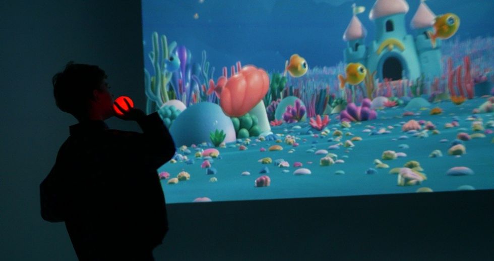 Silhouette of person with a glowing ball, watching colorful underwater animation on a screen.