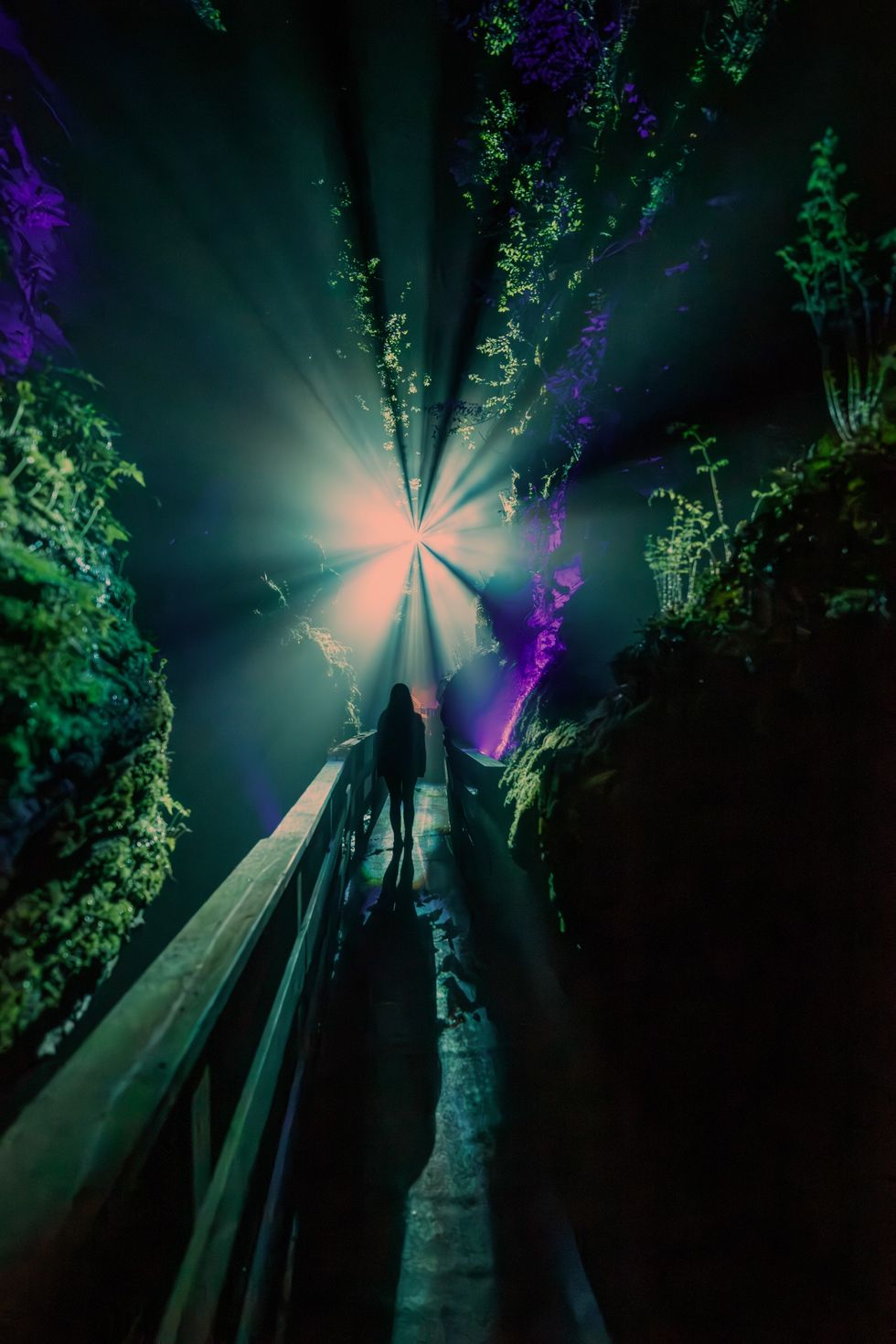 Silhouette on a walkway in a mystical, glowing cave with radiant light beams.