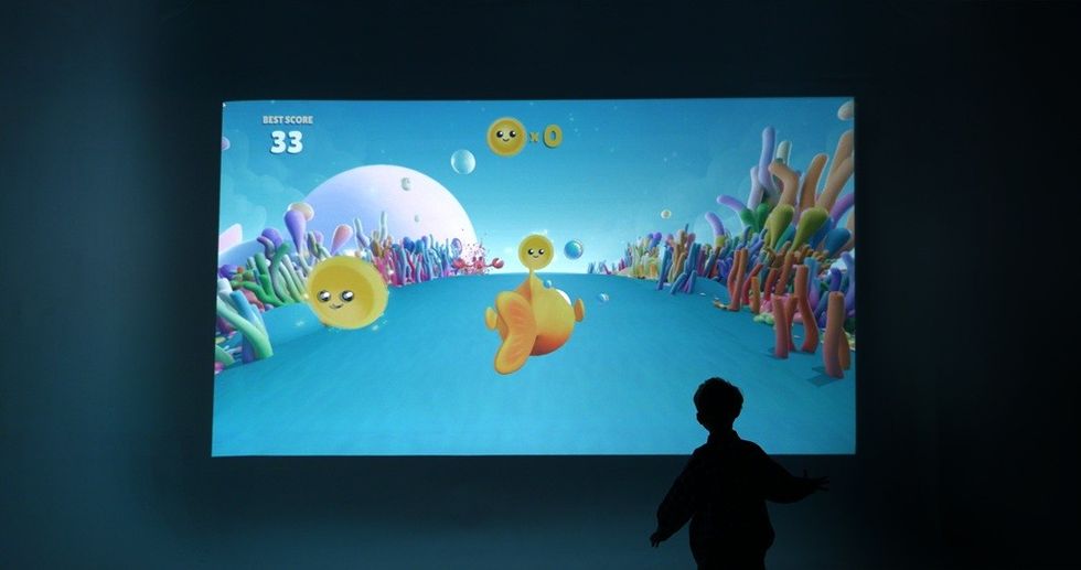Silhouetted child observes colorful underwater-themed video game on large screen.