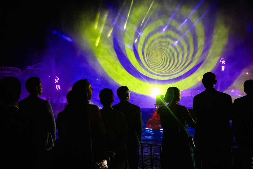 Silhouetted crowd watching a vibrant, swirling yellow and blue light show at night.