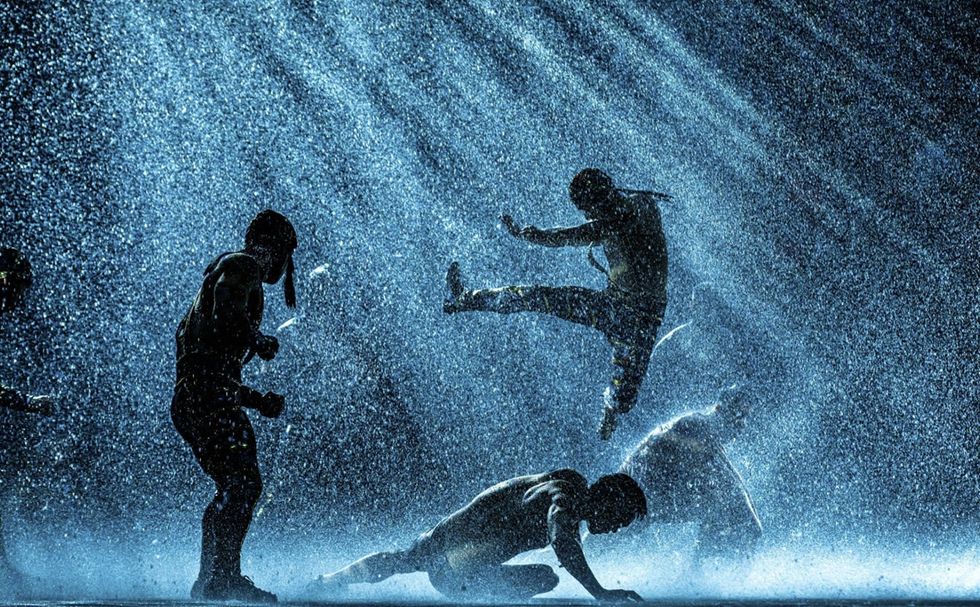 Silhouetted dancers perform dynamically in rain under dramatic lighting in The House of Dancing Water.