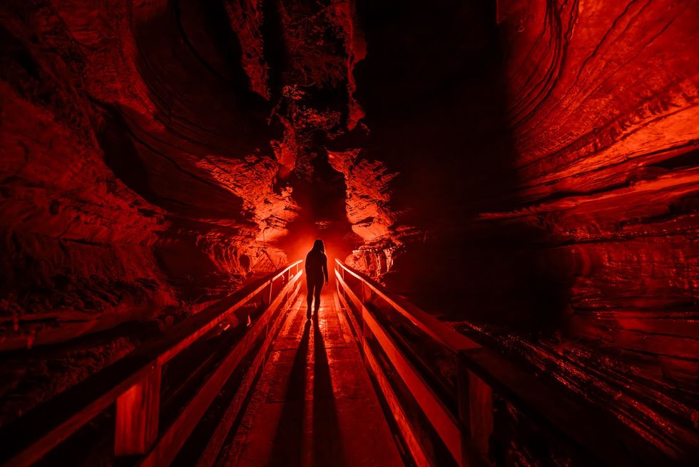 Silhouetted figure in a red-lit cave with dramatic shadows and rock formations.