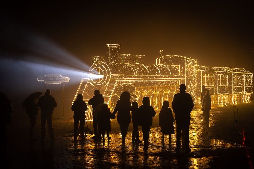 Silhouetted people admire a train made of glowing lights at night.