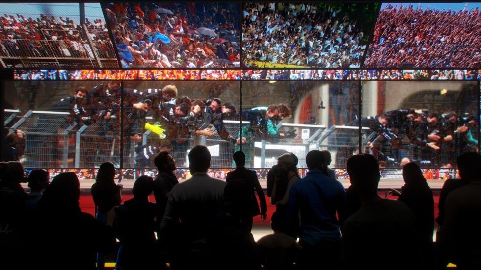 Silhouetted people watch sports scenes on a large, divided screen.