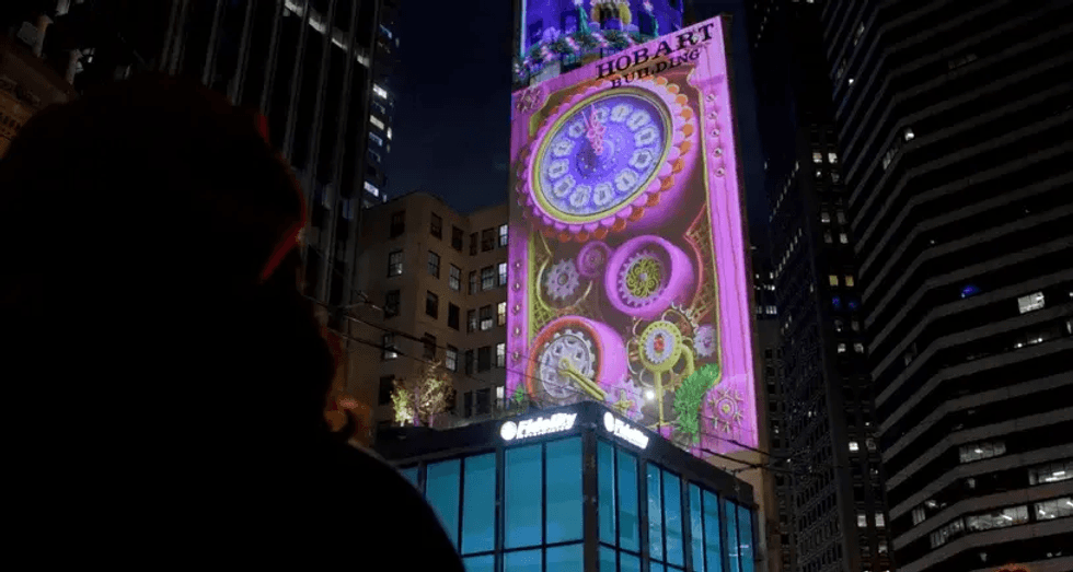 Silhouetted person watching colorful projection on tall city building at night.