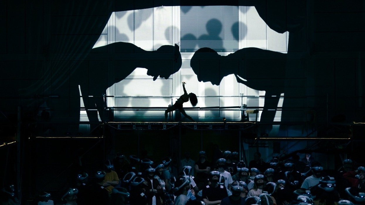 Silhouettes bowing above people wearing futuristic helmets in a dimly lit room.