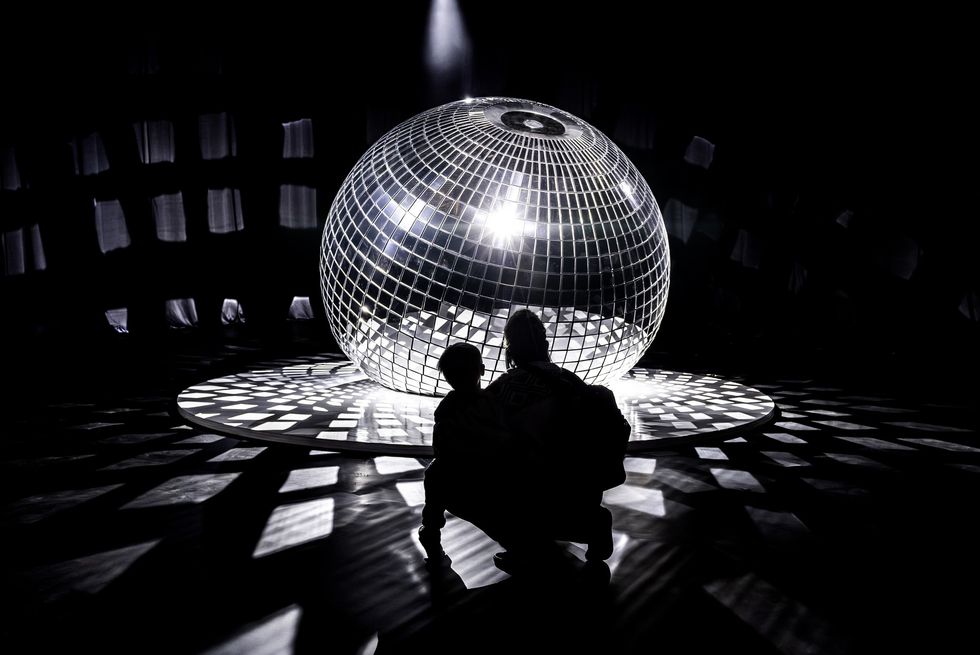 Silhouettes by a large illuminated disco ball in a dark room.