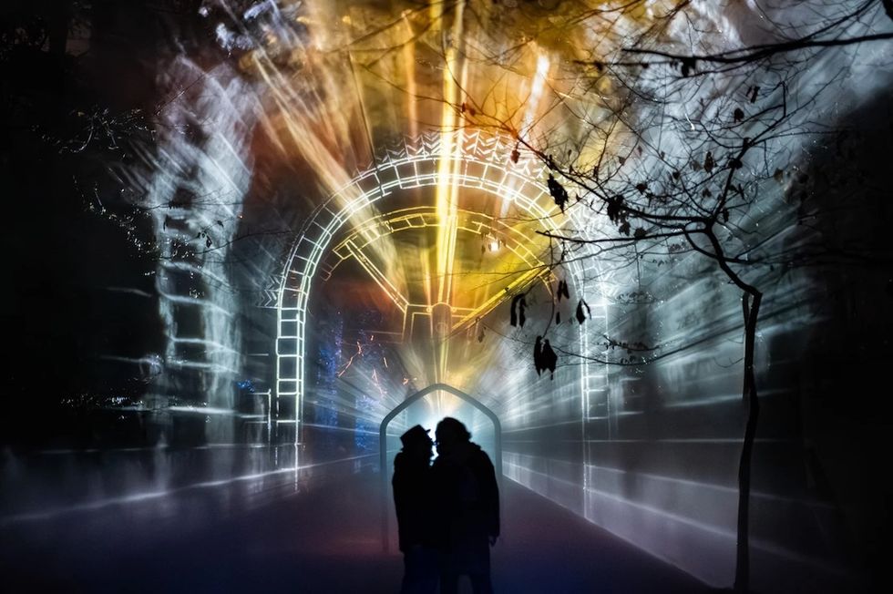Silhouettes near a glowing, colorful light tunnel at night.