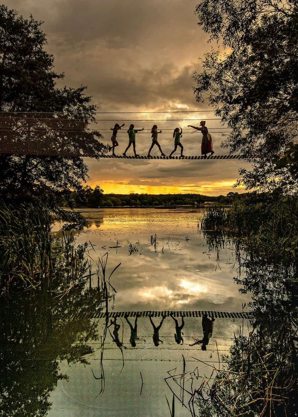 silhouettes of children on a rope bridge at the Skelf Island playground, Castle Howard, Yorkshire