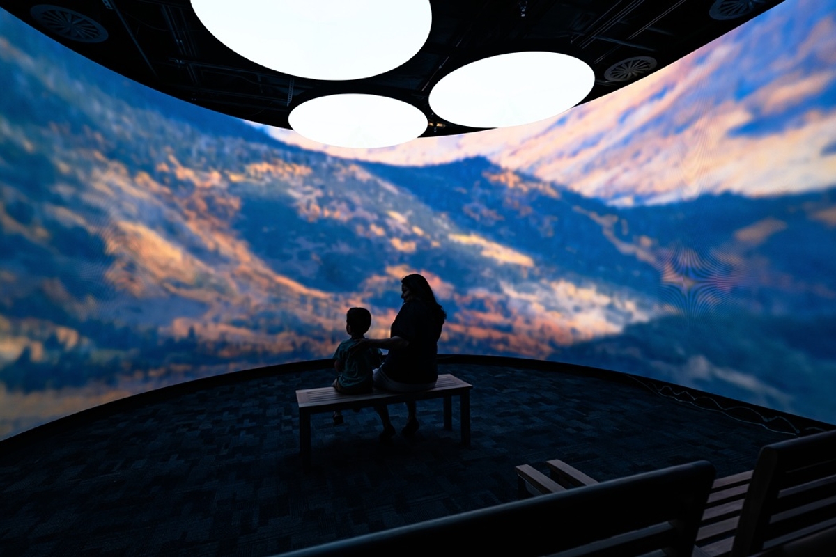 Silhouettes on a bench view mountain landscape projection in immersive room at Museum of Utah.