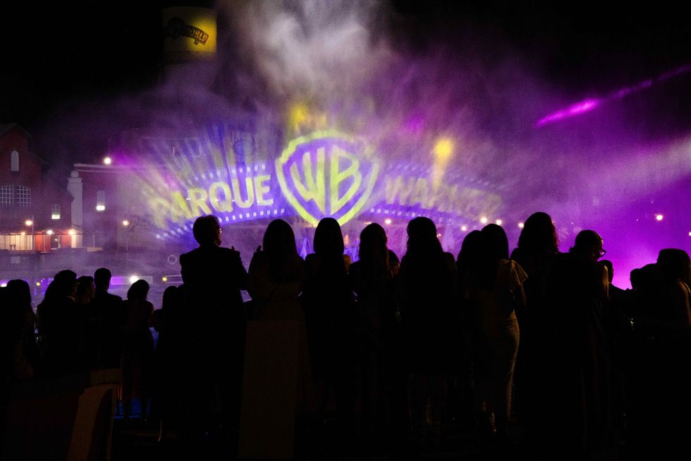 Silhouettes watch a colorful Warner Bros. logo projection on a misty night.