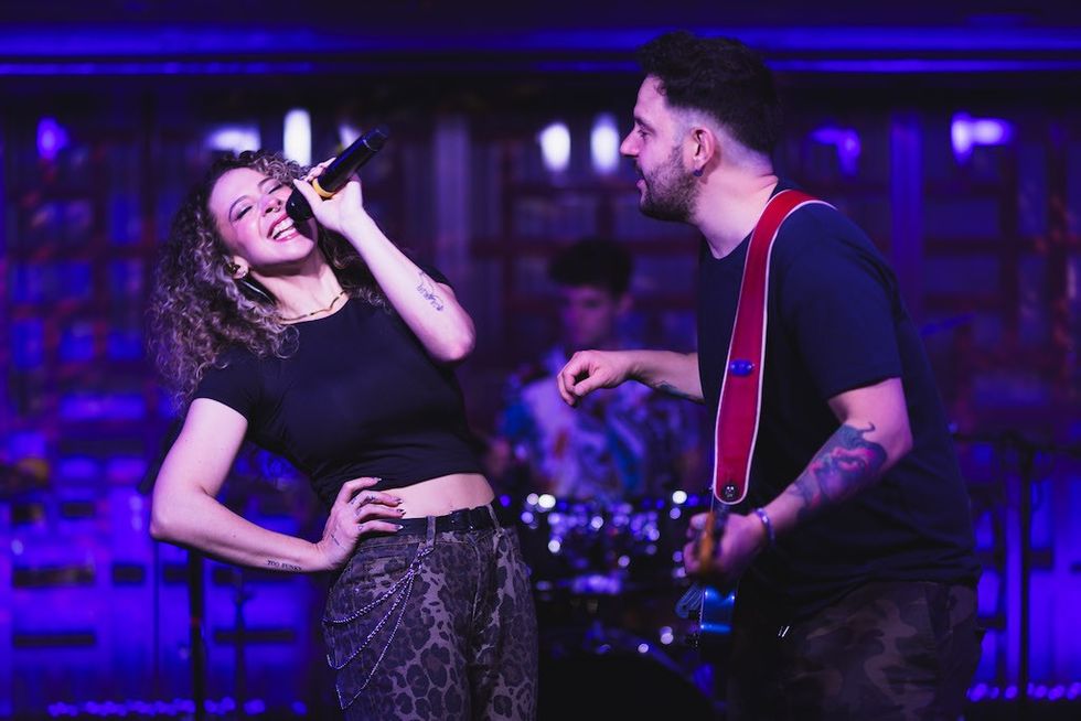 Singer and guitarist perform energetically on stage with purple lighting.