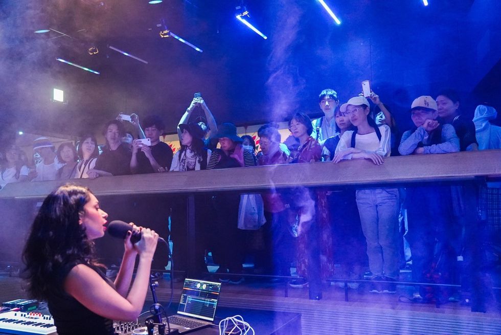 Singer performing on stage with an audience watching from a balcony above.