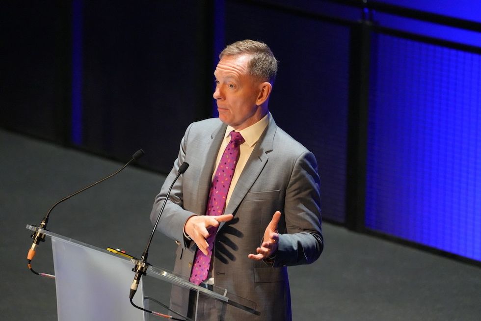 Sir Chris Bryant from the Department for Business and Trade speaks at a podium on stage with blue background.