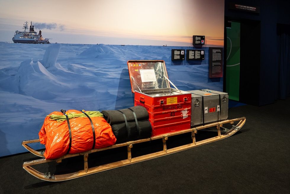 Sled with survival gear and boxes in an Arctic expedition display, ship and ice backdrop.