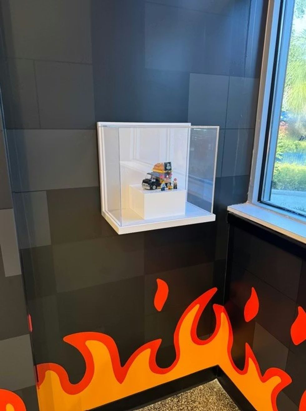 Small lego display case on black wall with flame design, near a window.