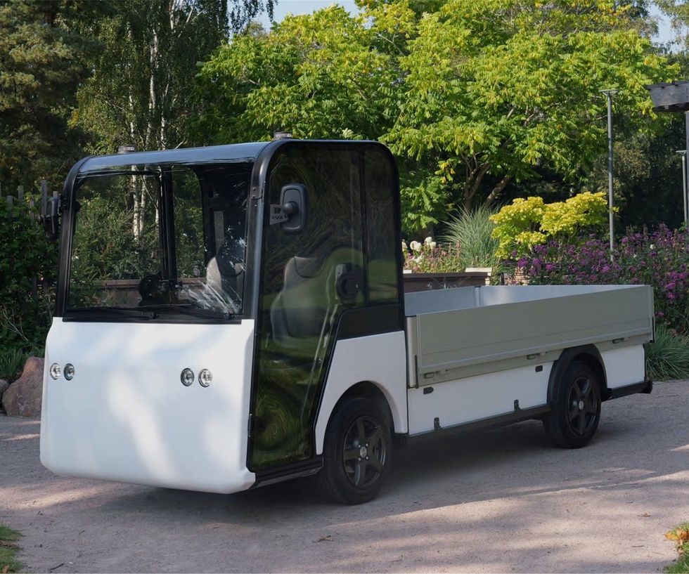 Small white utility truck parked on a garden path, surrounded by greenery.