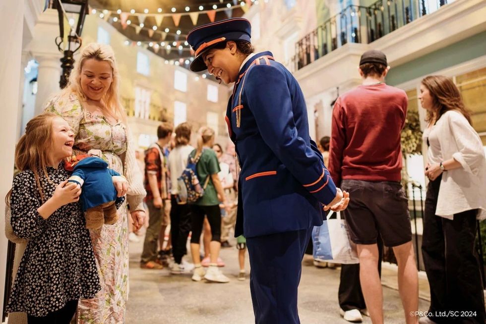Smiling child holds toy, interacts with person in blue uniform in lively indoor setting.