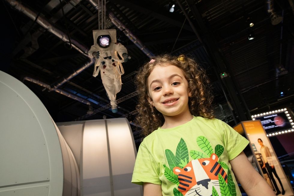 Smiling child in front of suspended astronaut suit at an exhibition.