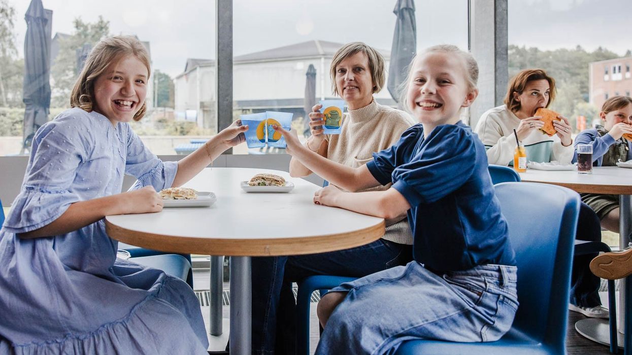 Smiling children in a cafe sharing a cheerful moment over a meal with adults in the background.