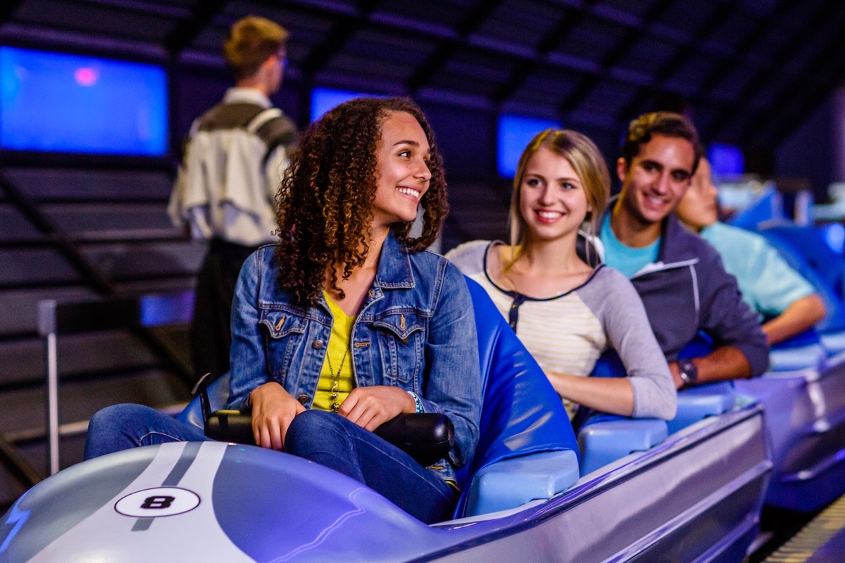 Smiling group seated on a futuristic ride in a theme park setting.