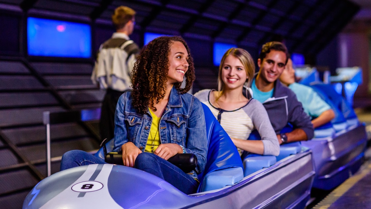 Smiling group seated on a futuristic ride in a theme park setting.