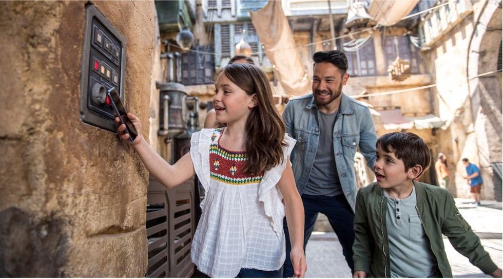 Smiling kids and man interact with a control panel at Disney's Star Wars: Galaxy's Edge land.