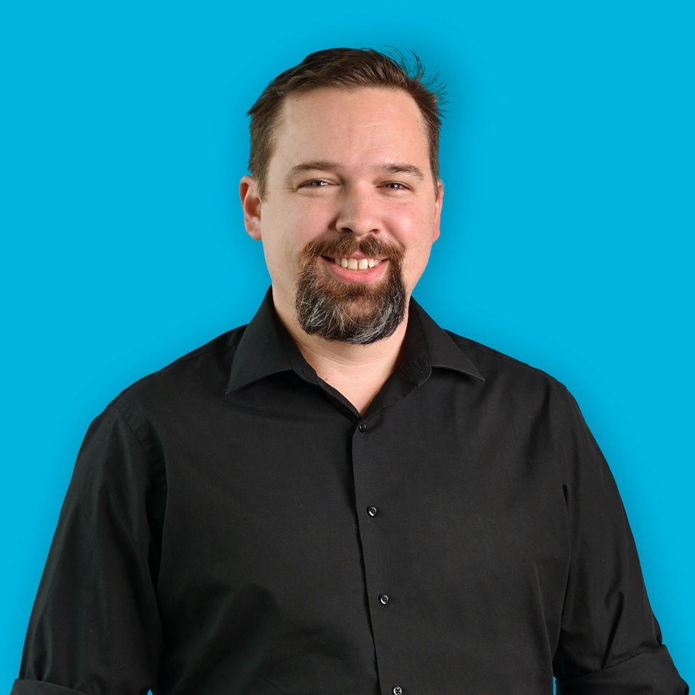 Smiling man in a black shirt against a bright blue background.