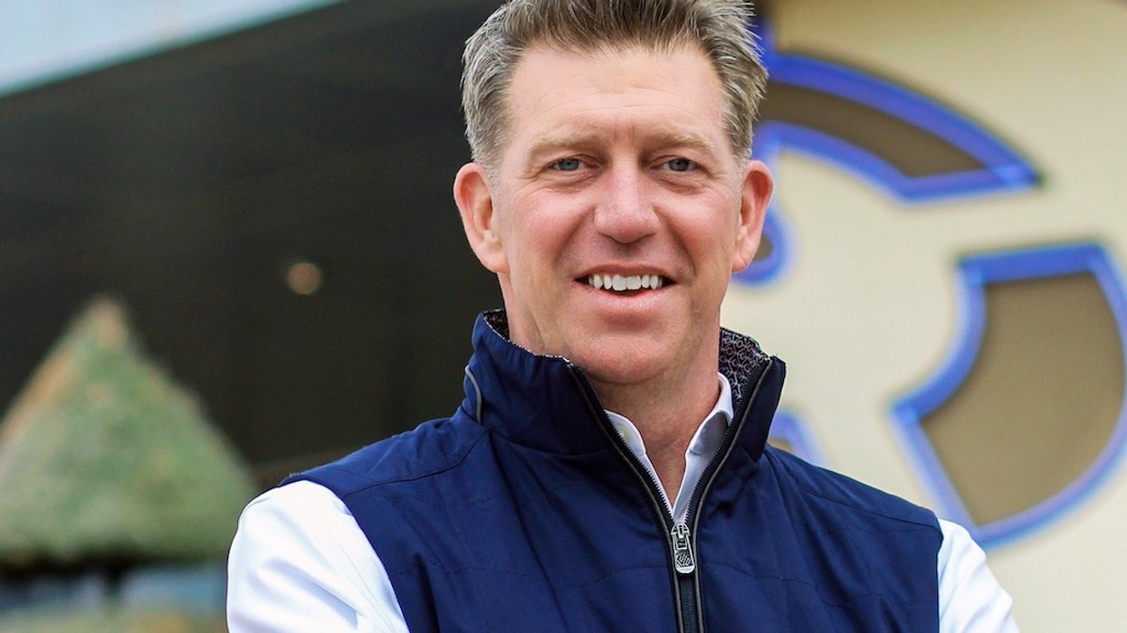 Smiling man in a blue vest outdoors, abstract background design.
