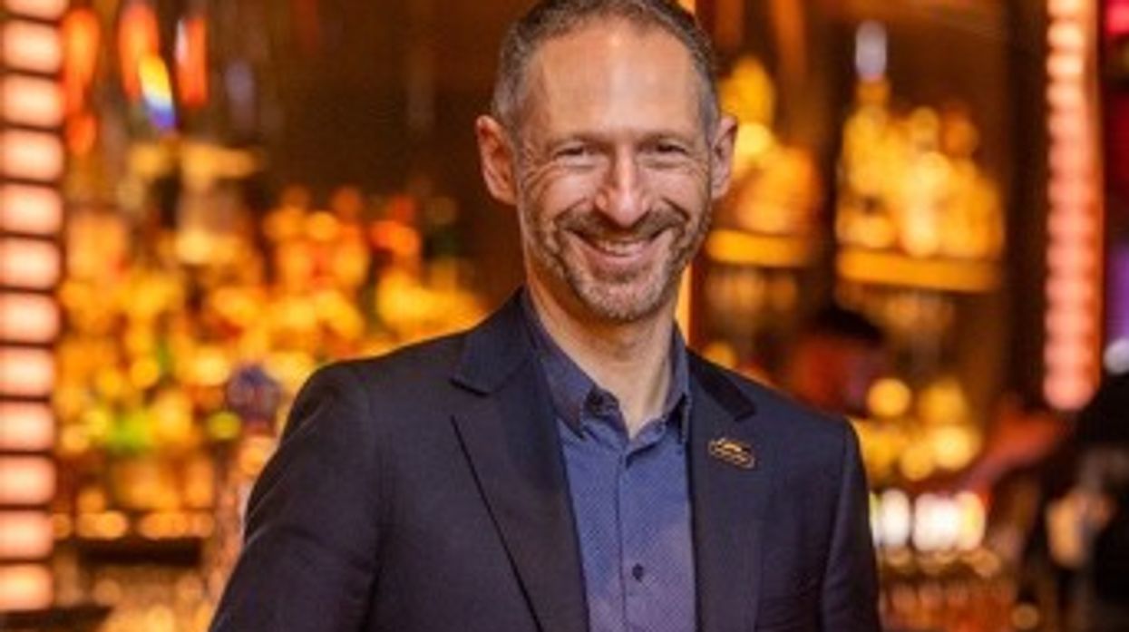 Smiling man in a suit standing in a warmly lit bar or restaurant.