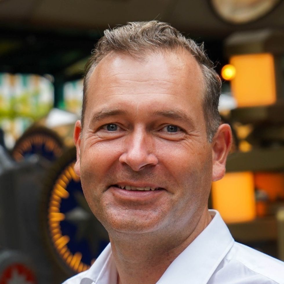 Smiling man in a white shirt with a blurred, colorful background.