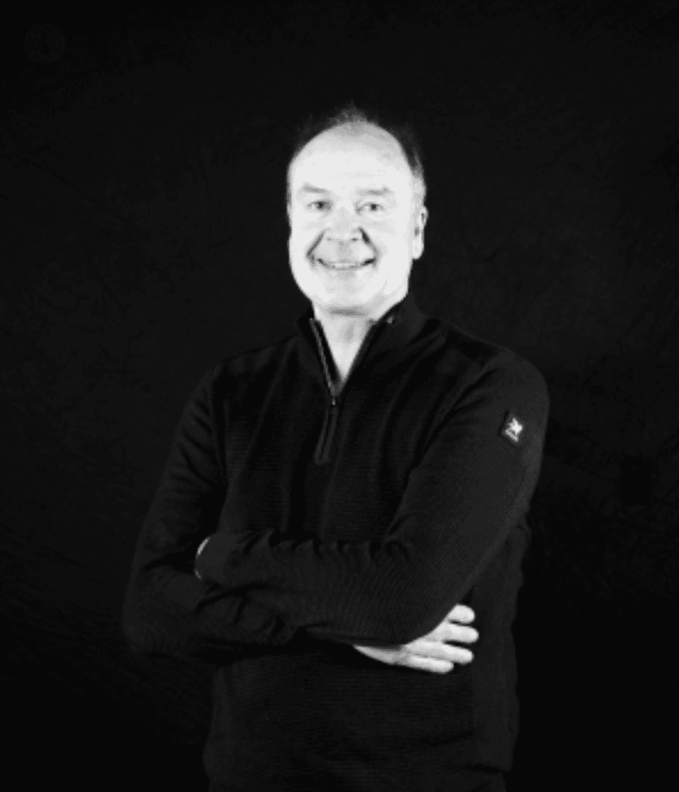 Smiling man in black sweater, arms crossed, against a dark background.