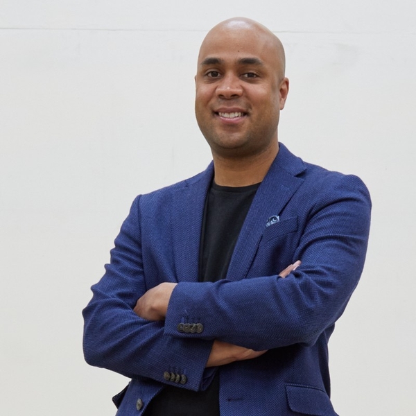 Smiling man in blue blazer with arms crossed against a white background.