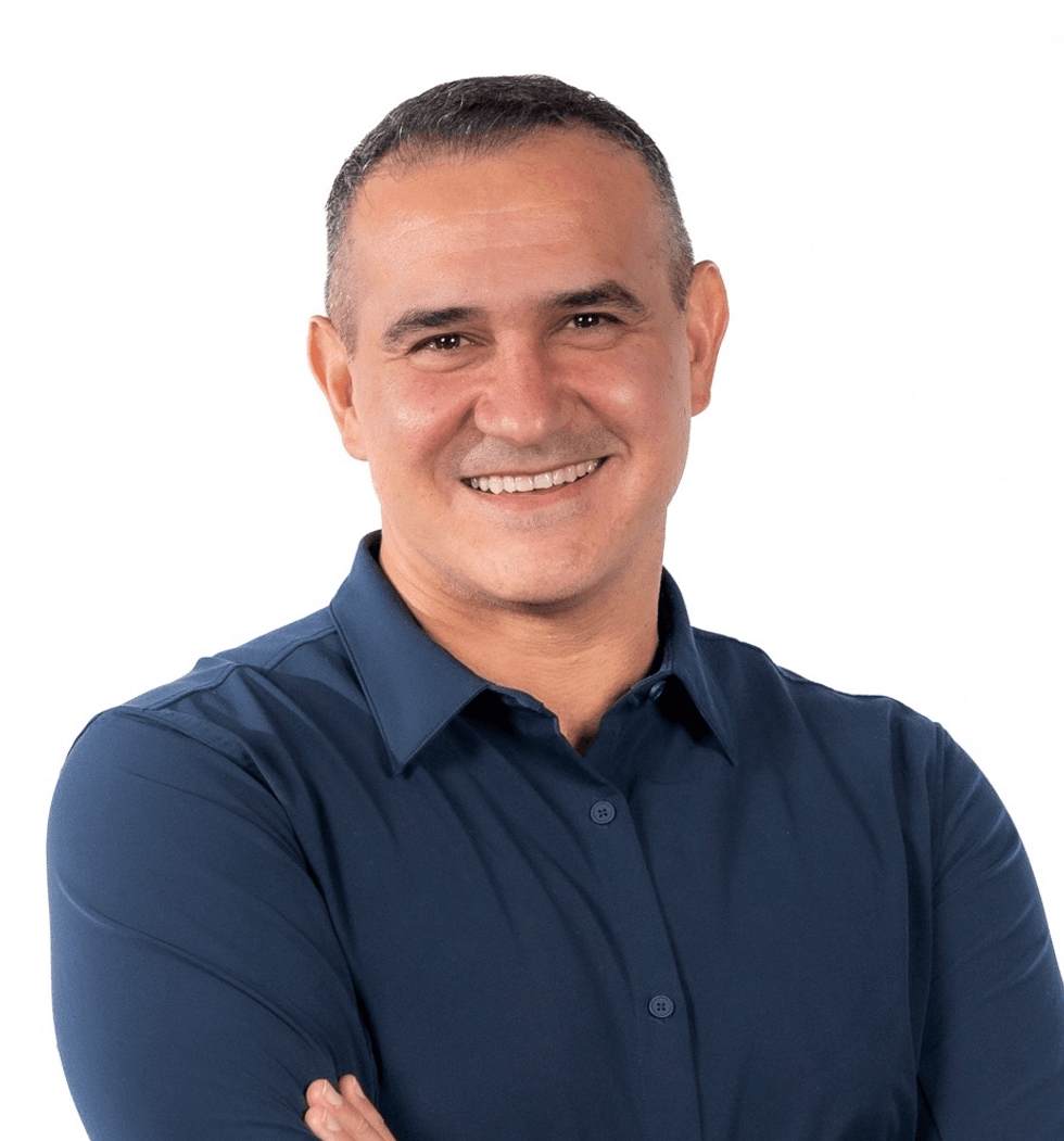 Smiling man in blue shirt with arms crossed against a white background.