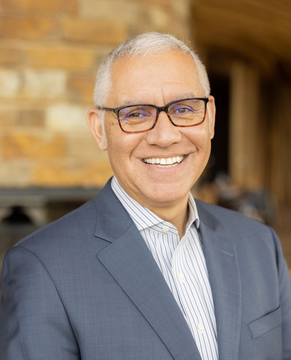 Smiling man, Julio Badin, in a suit and glasses against a blurred brick background.