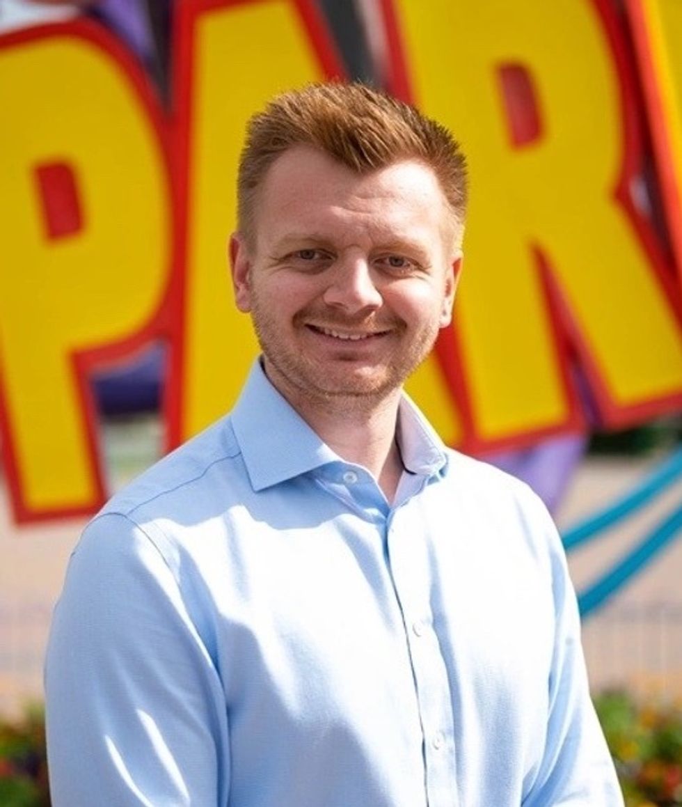 Smiling man, Lawrence Mancey, in blue shirt with colorful Paultons Park sign background.