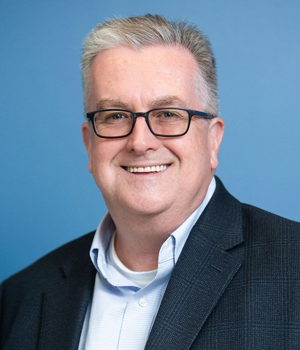 Smiling man named Sean McAllister, with glasses in a suit against a blue background.