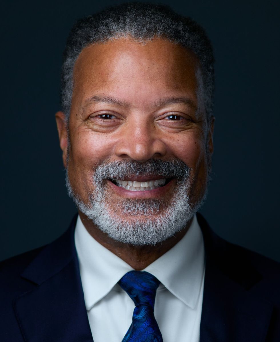 Smiling man \u200bnamed \u200bMike Blackman, with gray beard in a suit and blue tie, against a dark background.