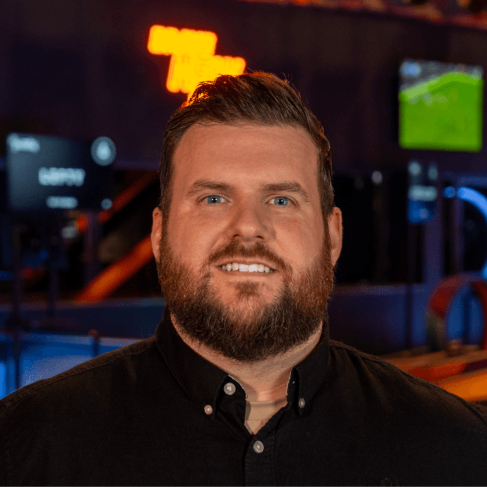 Smiling man with a beard in a dark shirt, blurred colorful background.