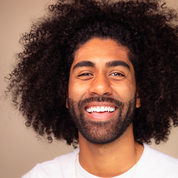 Smiling man with curly hair and a beard, wearing a white shirt.