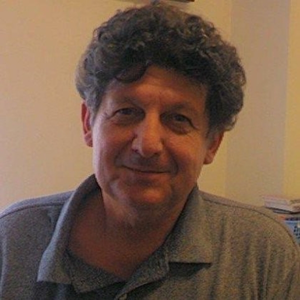Smiling man with curly hair wearing a grey polo shirt indoors.