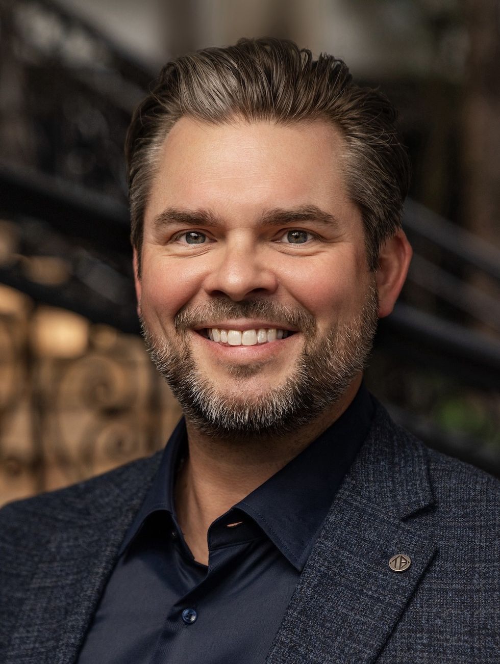 Smiling man with short hair and beard in navy suit jacket.