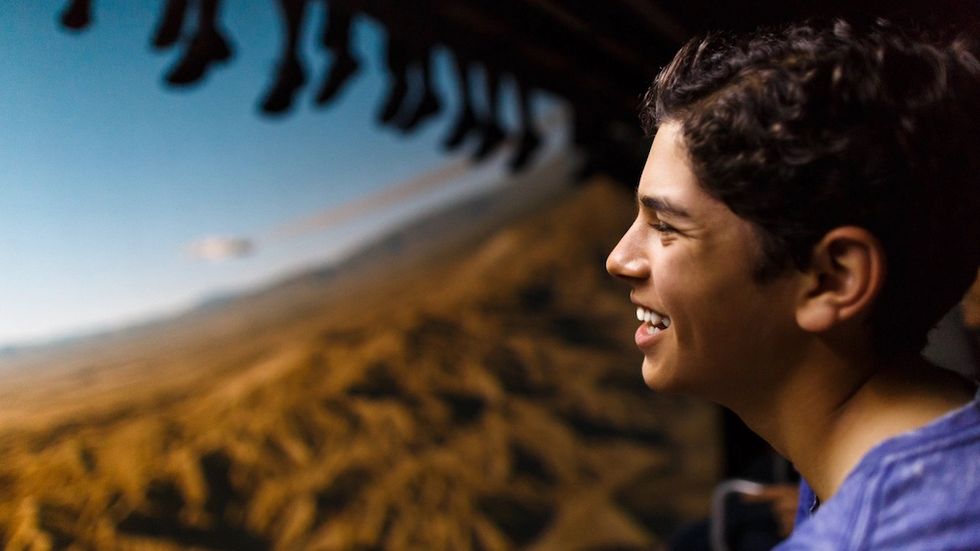 Smiling person enjoying a scenic flying ride with feet dangling above a landscape.