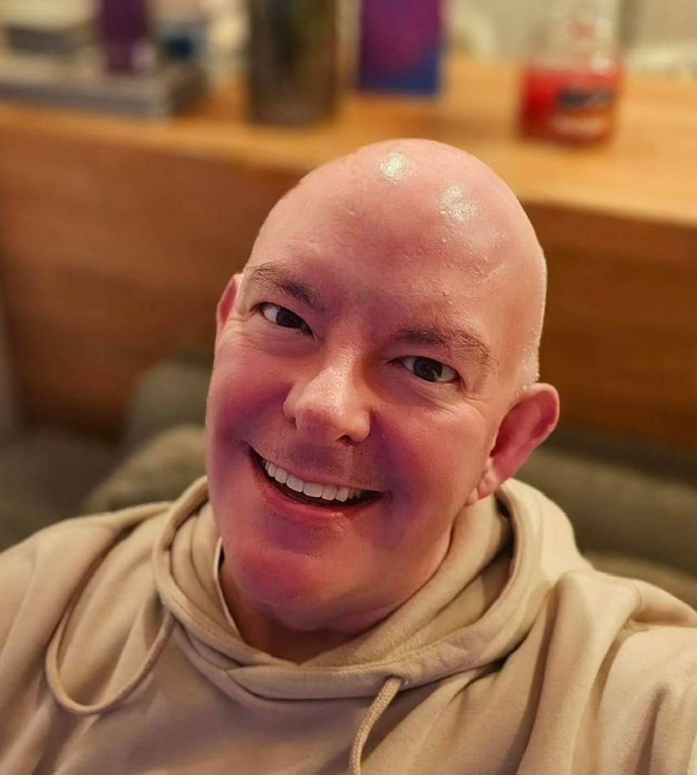 Smiling person in a hoodie named Ian Clappison, sitting on a couch with a wooden shelf in the background.