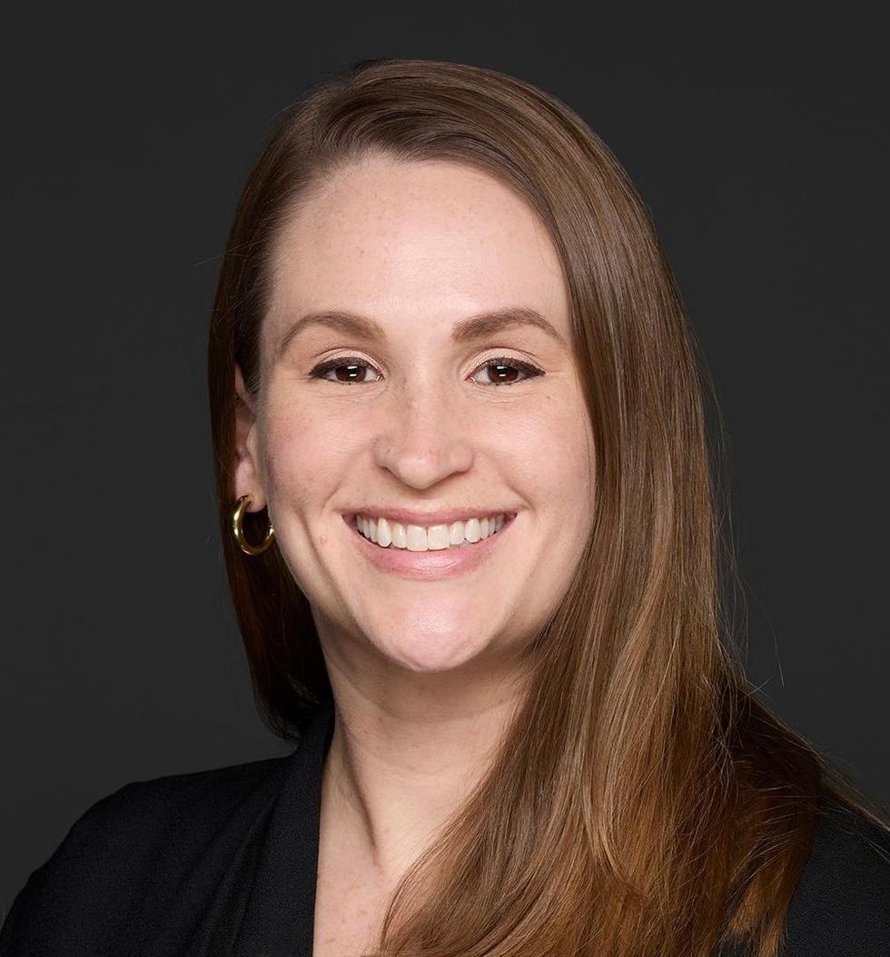 Smiling person, \u200bEmily Dunham, with long brown hair wearing a black shirt against a dark background.