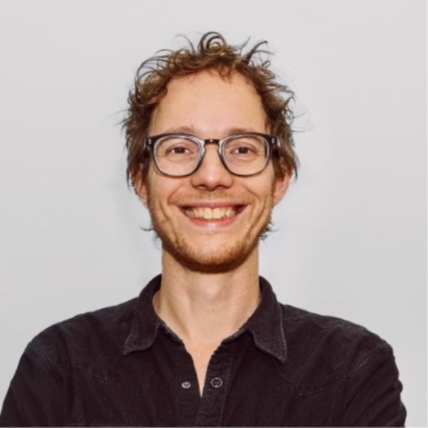 Smiling person with glasses wearing a black shirt against a plain background.