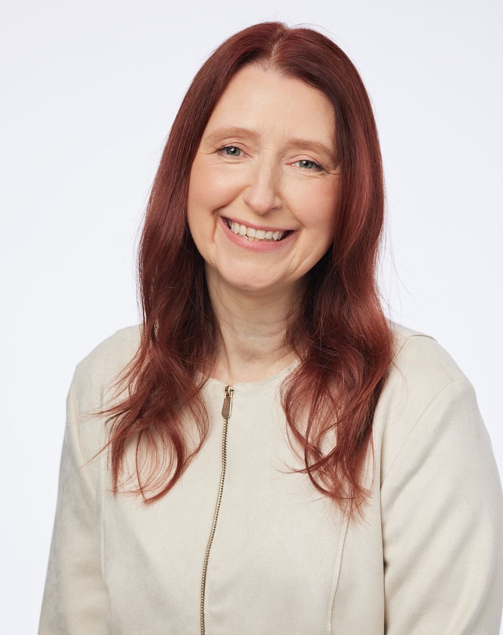 Smiling person with long red hair in a light beige jacket against a white background.