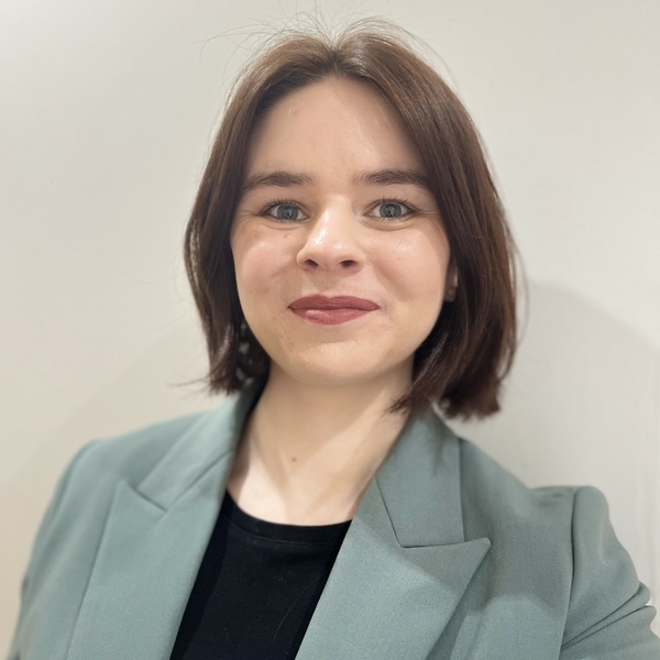 Smiling person with short brown hair in a gray blazer against a white background, named Alice Sarsfield-Hall.